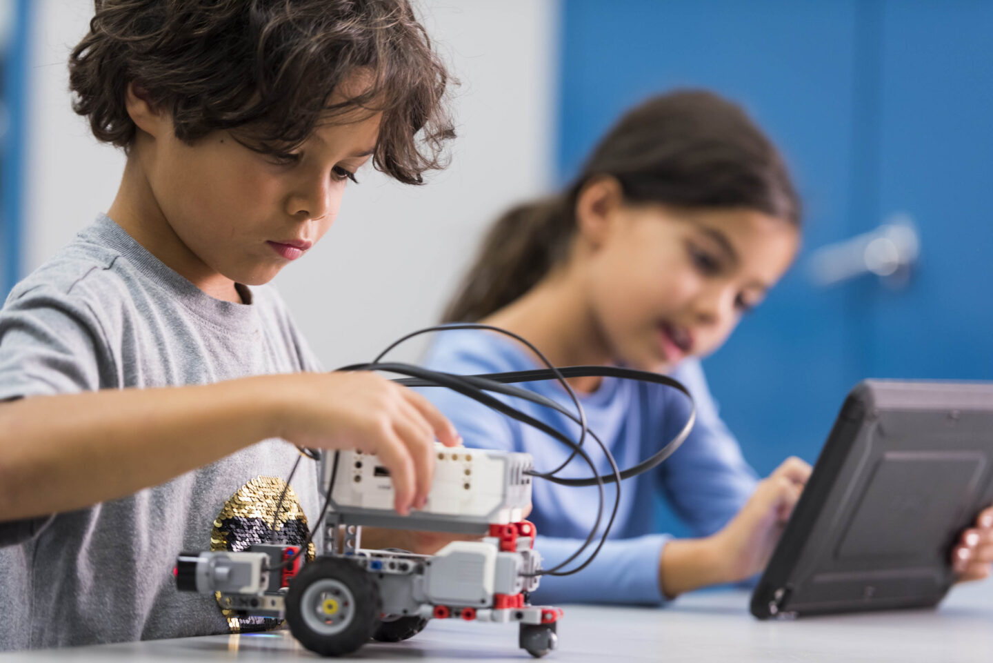Two children are conducting a science activity using a robot and a tablet