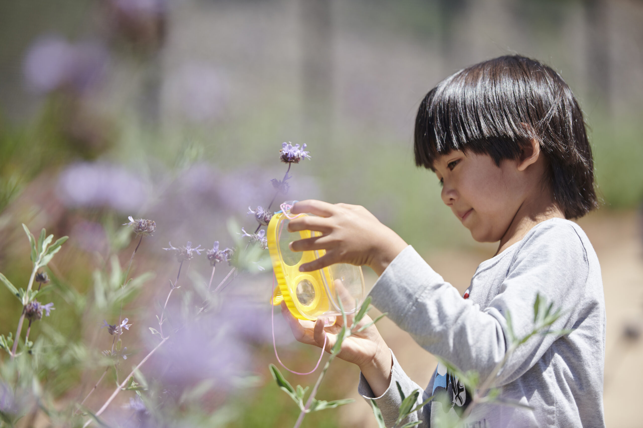 A child examines flowers using a yellow magnifying glass in the Outdoor Nature Lab.