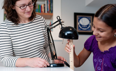 An adult and a student are measuring a lamp using a ruler.