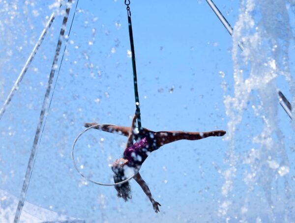 Trapeze artist performing with blurred water fountain water framing the artist