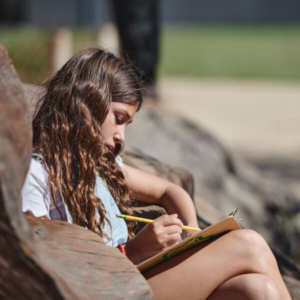 A youth sits outdoors and is writing during a nature journaling activity.