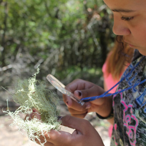 A student is outdoors examining nature through a magnifying glass