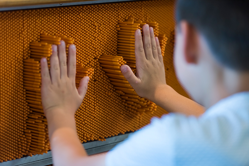 A visitor places their hands on the pin wall in the Young Explorers Area