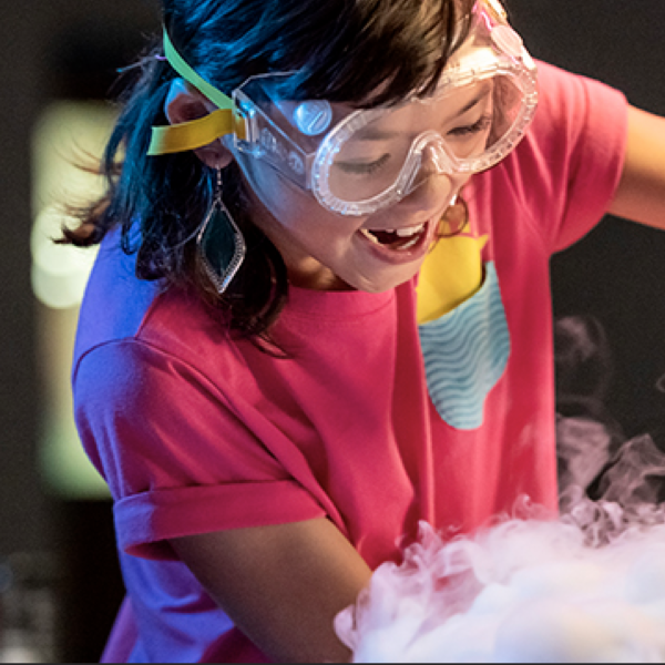 A youth pours liquid and wears safety glasses during a science demonstration