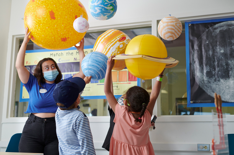 Two campers and a camp leader are holding up model planets as they make a model of the solar system.