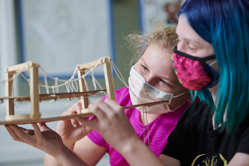 A student and an adult are holding up a model bridge that they have built.