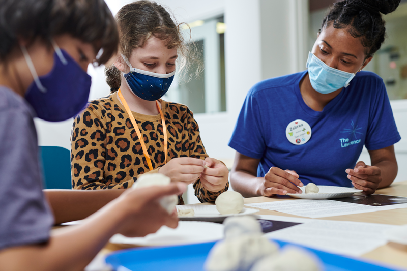 A teen intern is working with two campers while they create their asteroids.