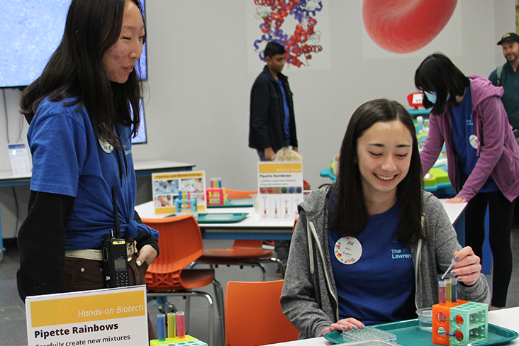 A volunteer is testing liquids during a science activity while another volunteer looks on